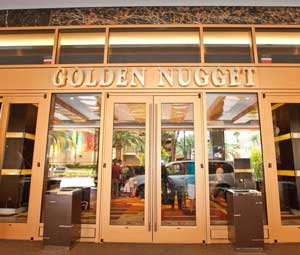 Set of gold colored front doors lead to a decadent hotel resort lobby. Above the doorway, large white-gold lettering reads "Golden Nugget".